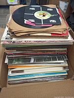 Top view of box filled with more than 50 used vinyl records, various covers and sleeves visible
