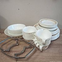 Corelle Livingware dish set items arranged showing plates, bowls, cups, and metal trivet stand.