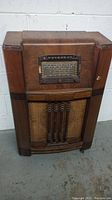 Full front view of antique Rogers radio console showing the wooden cabinet with speaker grille and tuning panel with control knobs.