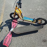 Yellow Throttle brand scooter with front and rear wheels, black skateboard, and pink waveboard on asphalt surface