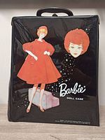 Front of black vinyl Barbie doll case showing 1960s style illustration featuring Barbie in a red flare dress and a close-up face portrait with 'Barbie Doll Case' text.