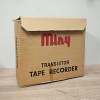 Original cardboard box of the Miny transistor tape recorder with visible wear and some tape marks.