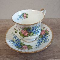 Side view of the teacup placed on the saucer showing floral patterns and gold trim.