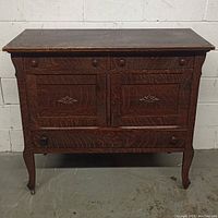 Full front view of solid wood antique dresser showing decorative carved details, curved legs with casters, and wood finish.