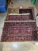 Four area rugs partially rolled and laid on floor showing overall condition including frayed edges and wear.