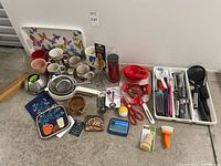 Photo of full assortment of various kitchen items including mugs, utensils, bowls, coasters and containers arranged on floor