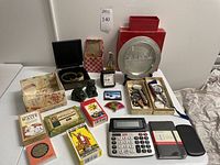 Photo of assorted items on table including decorative pewter plate, magnifying glasses in boxes, jade foo dogs, tarot cards, calculators, magnets and address book.