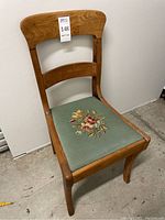 Front view of wood chair with green needlepoint seat with floral embroidery