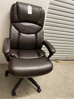 Front angled view of brown leather look office chair showing padded seat, backrest, armrests, and caster wheels.