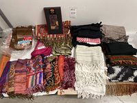 Top view of approximately two dozen scarves laid out showing variety of colors, patterns, and textures, including multi-colored woven and fringed scarves and solid color scarves.