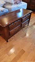 Full view of cedar chest showing wooden top and faux drawers with metal handles, placed on hardwood floor beside bed.