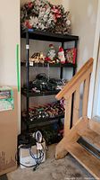 Shelving unit with assorted faux garlands, wreaths, holiday figurines, hanging ornaments, and piles of green wired Christmas lights.
