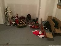Photo showing the full collection of Christmas decorations arranged on the floor including Santa figures, wreaths, hats, stockings, and other decorations.