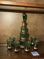 Photo showing the full green glass decanter with stopper surrounded by six matching liquor glasses, all with silver bands.