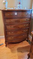 Front view of the solid wood five-drawer dresser showing brass-tone handles, curved drawer fronts, and cabriole legs.