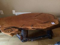 Oblique view of table showing live-edge wood slab top and tree branch legs coated in epoxy resin