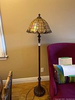 Full view of the stained glass floor lamp showing the height and base near a wall and furniture.