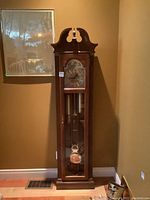 Full view of tall wooden grandfather clock in room corner showing overall height and design.