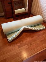 Rolled and partially unrolled egg crate memory foam bed topper showing textured surface and color.