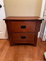 Front view of the wooden nightstand showing two drawers with black metal handles and a medium-tone finish.