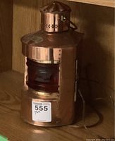 Front and side view of metal railway style lamp with red glass lens on wooden shelf.