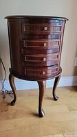 Front view of small wooden side table showing four curved drawers with brass knobs and cabriole legs.