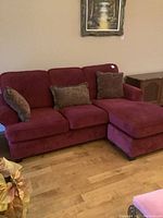 Red sofa with ottoman and three decorative pillows in a living room with wooden floor and sideboard in the background.