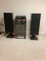 Front view of stereo cabinet with turntable, amplifier, tape deck, tuner, and speakers on stands.