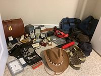 Lot overview showing men’s extra large brown hat, sandals, grooming sets, tote bags, wristwatches, umbrella and accessories scattered on carpeted floor.