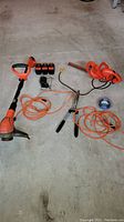 Photo of Black and Decker Grass Hog trimmer, batteries, electric saw, extension cords, trimmer line spool, and hedge clippers on concrete floor.