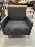 Front view of the cushioned armchair showing dark fabric with small white dots, angled wooden legs, and cushioned seat and armrests.
