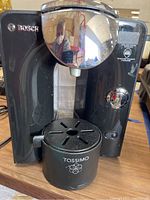 Front view of Bosch Tassimo coffee maker showing chrome front with Bosch logo, control dial, power button, and Tassimo drip tray.