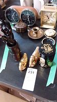 Lot showing two clocks, brass candle holder, wooden container, ceramic jar, brass figurines, and small items on black table surface