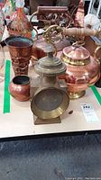 Overview of all items in the lot including copper teapots, vase, bowl, and brass lantern on table.