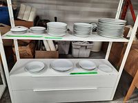 Full view of shelves with stacks of white dishes including plates and bowls of various sizes.