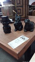 Photo of three black carved figures: hunter, human figure, seal on wooden table.