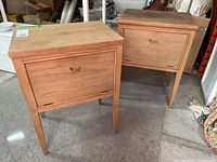 Two wooden nightstands side by side showing the front and top surfaces, highlighting the natural wood finish and pull-down door storage.
