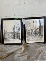 Photo showing both framed prints together, one of an archway (Porte St Louis) and the other a street view (Vieux Montreal). Both prints are in black wooden frames with minor scuffs.