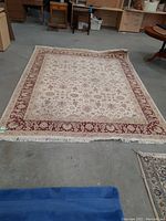 Full view of the machine made wool area rug with floral and paisley motifs and fringe.