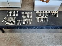 Overhead view of full flatware set arranged on black surface showing spoons, forks and knives