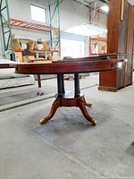 Side view of round wood dining table showing pedestal base with four legs ending in brass caps