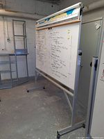 Side view of whiteboard with metal frame on wheels showing writing on the board and one of the rolled maps on top.