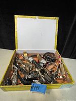 Photo of an open box containing a pile of various men's and women's wristwatches with mixed metal and leather bands on a flat surface.