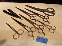 Photo showing seven pairs of vintage and antique scissors and one safety razor. All metal with varying sizes and styles, showing age wear.