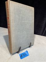 Front and spine of the antique hardcover book showing the light cloth cover and red text on spine, displayed on a book stand.