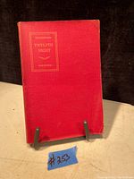Front cover of antique book showing red cloth hardcover with gold embossed title 'Shakespeare's Twelfth Night'. The book is standing upright on a display stand.