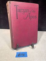 Front cover of the red hardcover book titled Tarzan of the Apes showing wear on spine and edges.