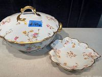 Front angle showing tureen with lid and matching dish side by side, highlighting floral and gold pattern.