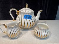 Antique tea set with teapot, creamer, and sugar bowl in white ceramic with gold and black diagonal stripes.