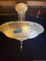 Ceiling fixture mounted showing the large detailed glass shade with floral and geometric designs on rim and center, finial at bottom